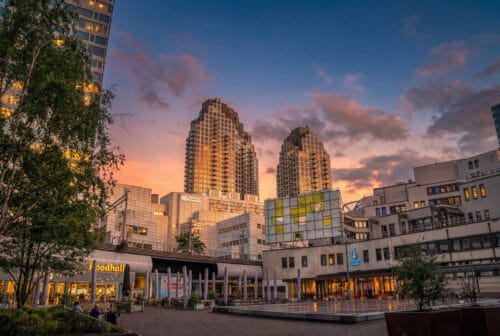 De twee Grotius-woontorens (New Babylon) in Den Haag met verlichte gevels bij zonsondergang, gezien vanaf het plein met de Foodhall