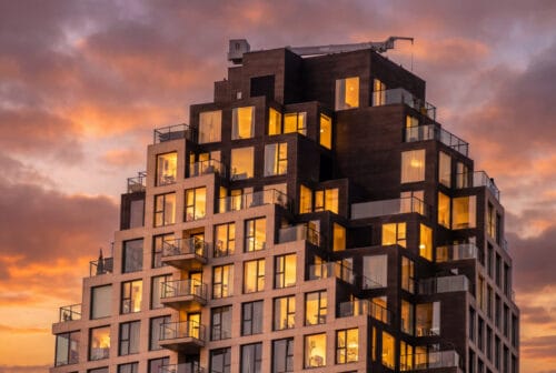 Detailopname van de getrapte top van een Grotius-woontoren met verlichte ramen en balkons bij avondrood