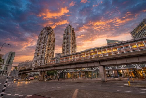 De Grotius-torens in Den Haag achter het stationsviaduct bij een kleurrijke zonsondergang, met de weg op de voorgrond
