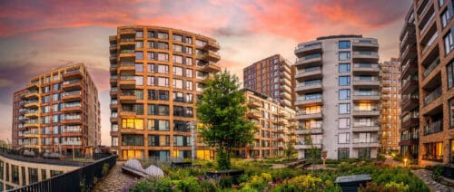 Panorama van woningbouwproject Zaanse Helden met bakstenen en witte appartemententorens rond een groene binnentuin bij zonsondergang